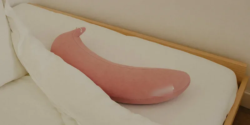 Slim curved pregnancy pillow tucked under a duvet