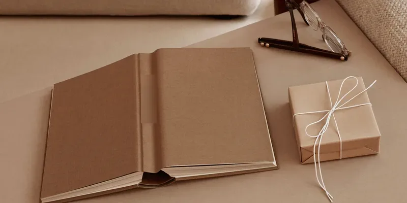 Brown book beside a kraft wrapped gift and glasses