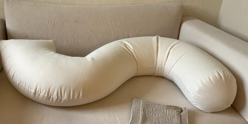 C-shaped nursing pillow on a sofa with a baby blanket