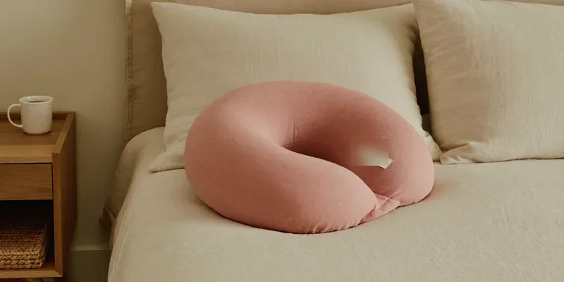 C-shaped pregnancy pillow in dusty rose on a made bed