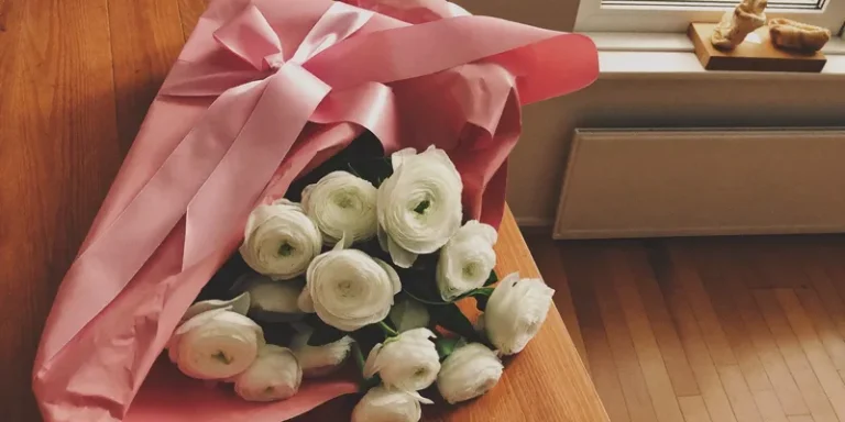 Pink wrapped gift beside white ranunculus flowers