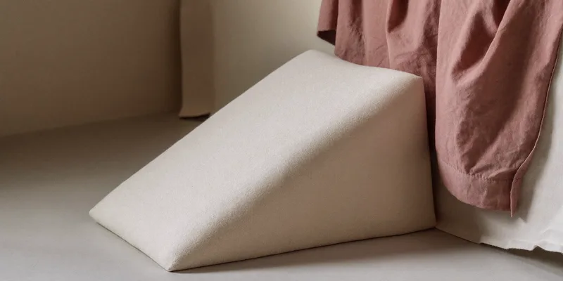 Small incline wedge cushion with soft cover on a bed