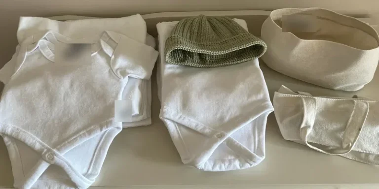 Plain newborn onesies, hat and swaddle beside a bag