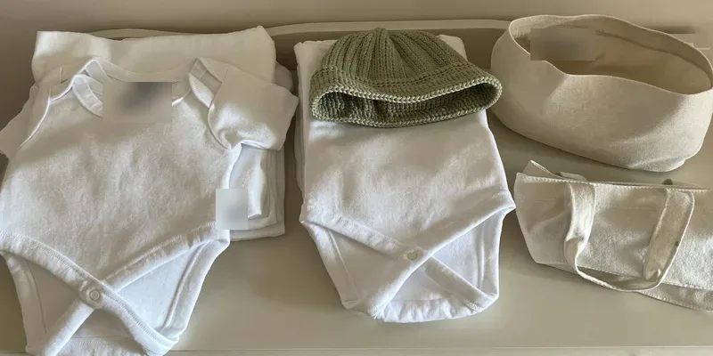 Plain newborn onesies, hat and swaddle beside a bag