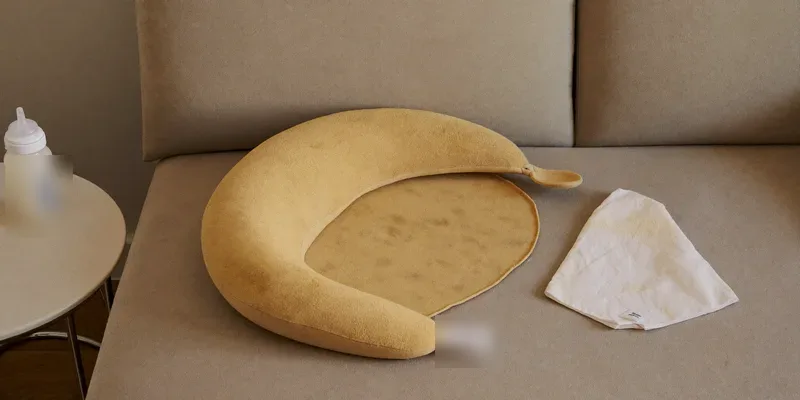 Plain nursing pillow on a sofa with baby bottle