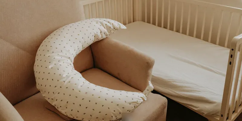 Nursing pillow on a chair with an empty crib behind