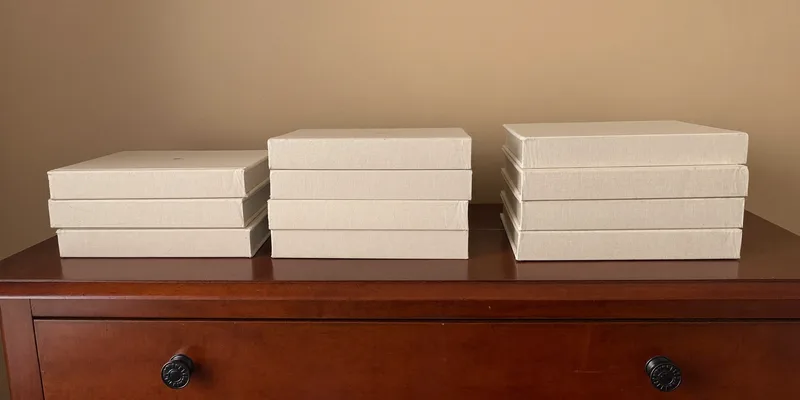 Three growing stacks of plain books on a dresser