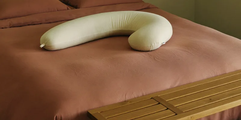 Contoured knee pillow and curved pregnancy pillow on a bed