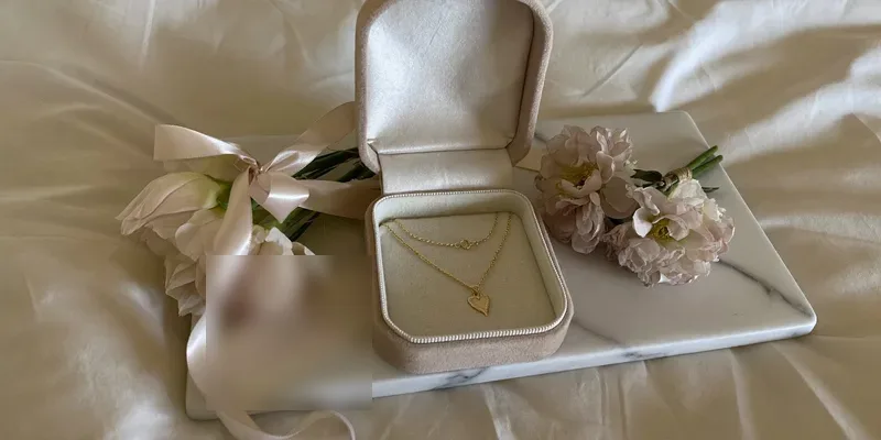 Open jewelry box with a gold necklace and peonies