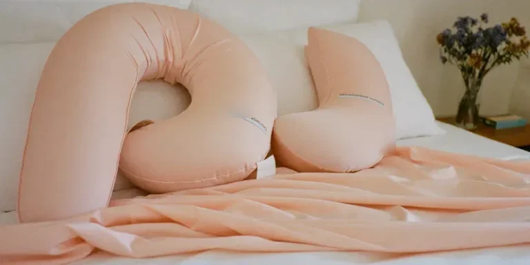 Blush pink U-shaped pregnancy pillow on white bedding