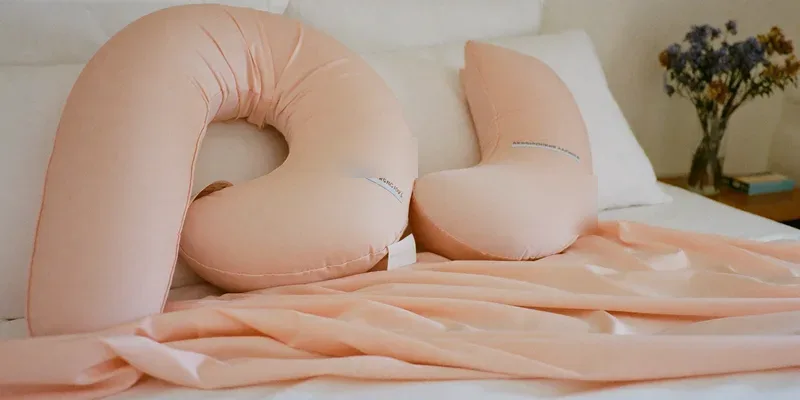 Blush pink U-shaped pregnancy pillow on white bedding