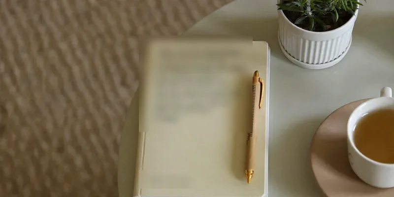 Closed notebook with a pen, tea and a plant
